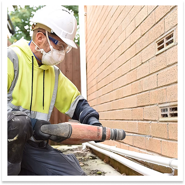 a man removing insulation from a cavity wall. He is wearing a mask , hard hat and high visibility jacket